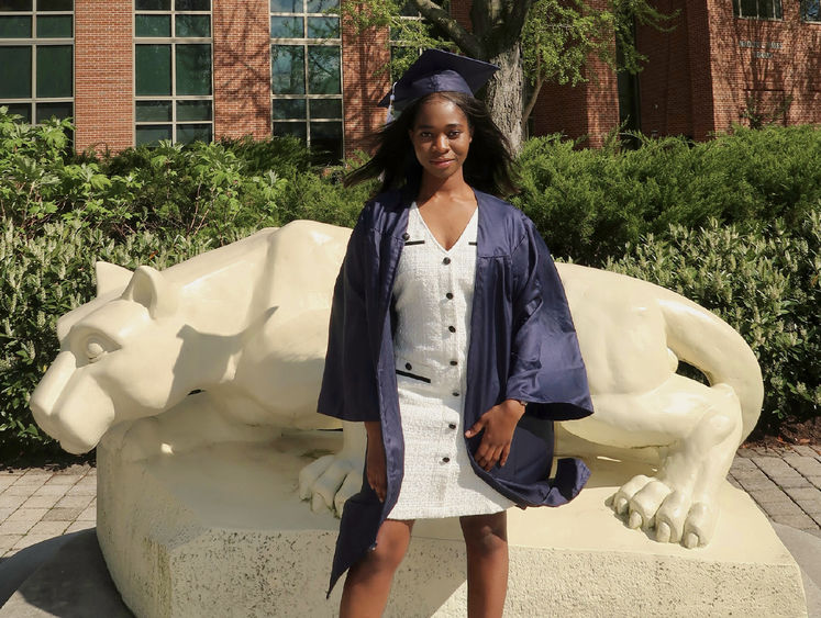 Mary Odei wears her cap and gown in front of the Nittany Lion statue at Penn State Harrisburg