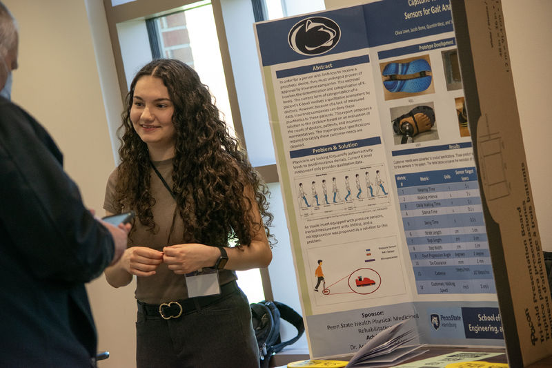 A student stands next to a research poster at the Capstone Design Conference