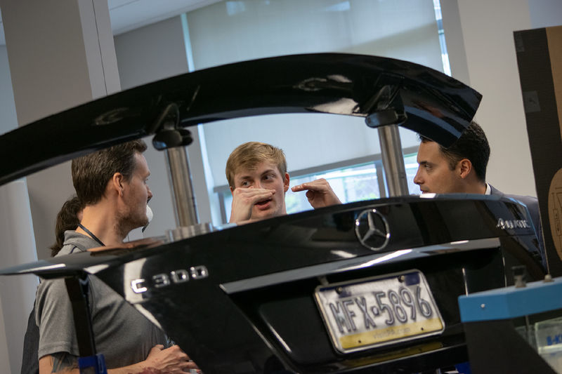 Students and faculty talk in the background of a car trunk lid on display