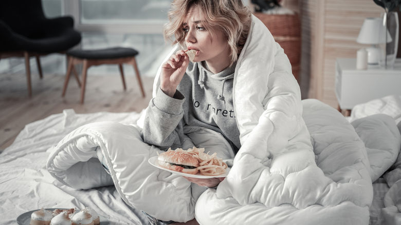 A woman eating ice cream looking sad and wrapped up in a blanket