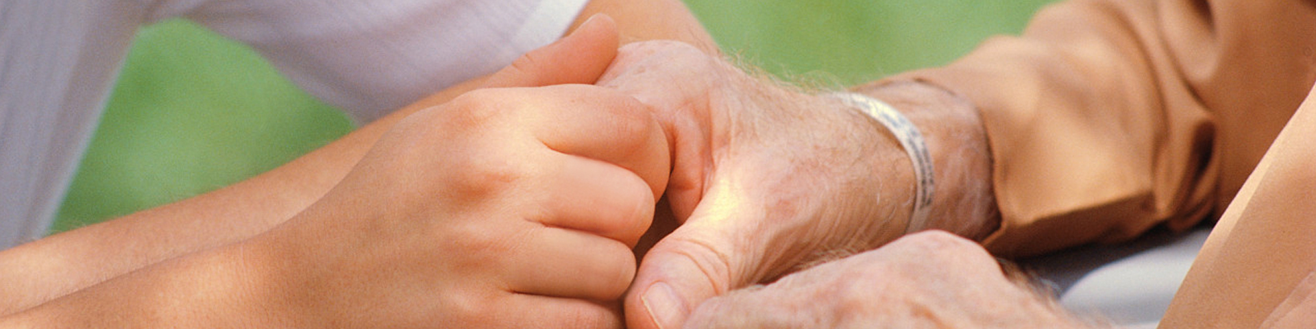 A younger man's hand holds that of an older person in a comforting manner