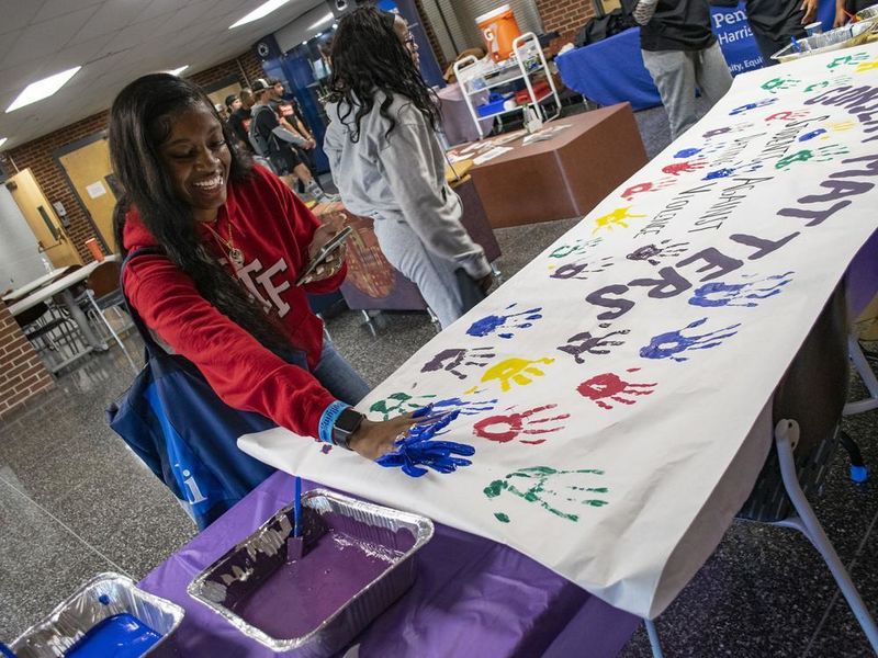 A student presses her hand, painted blue, on a banner with the words "Consent Matters."