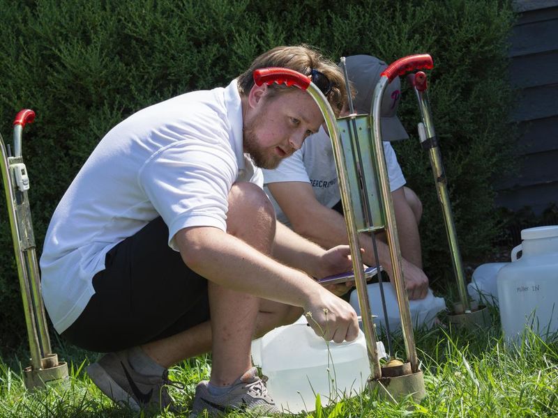 Two men pour water into a device planted in the ground to measure infiltration rates