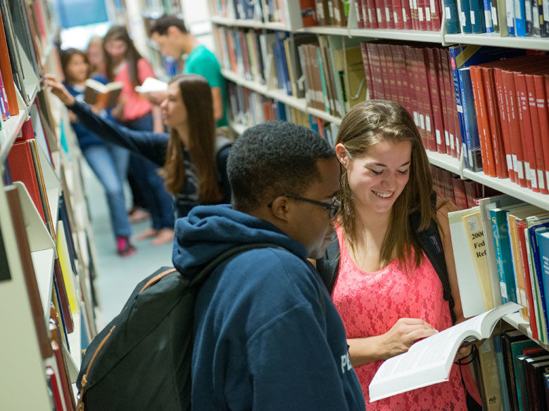 students work together among library bookshelves