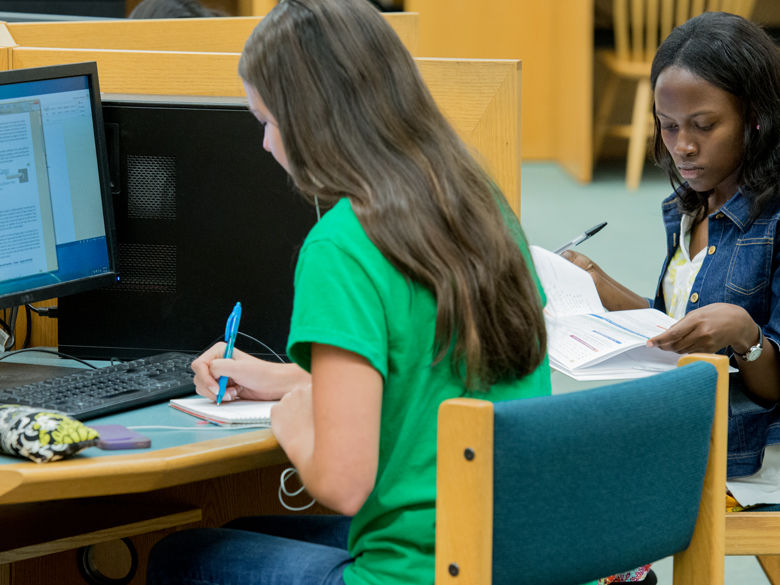 Two female students studying and taking notes in the library