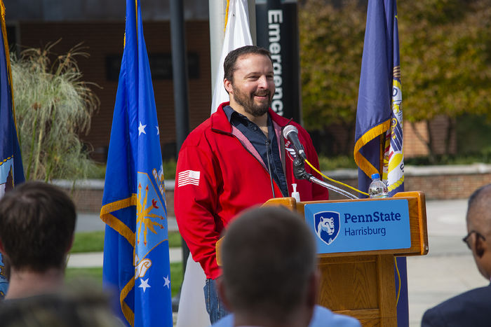 Photo of Ryan Allman, standing behind a lecturn and in front of flags during a 2021 Veterans Day ceremony 