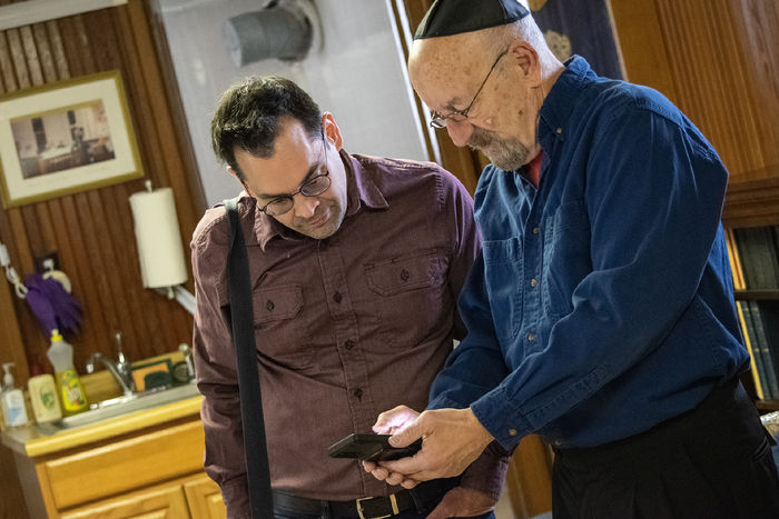 Two men stand together, with one showing a cell phone photo to the other