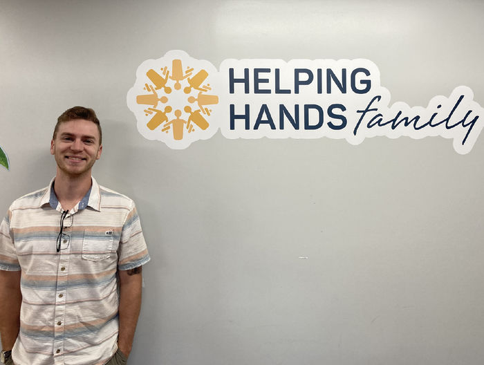 Jeremy Katz stands in front of a wall with the Helping Hands Family logo