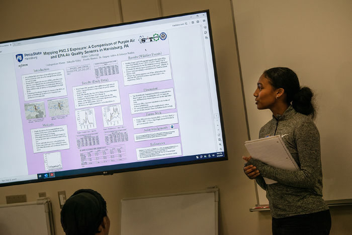 Ariam Gebrezgi stands next to a big screen showing her research project for the EnvironMentors program