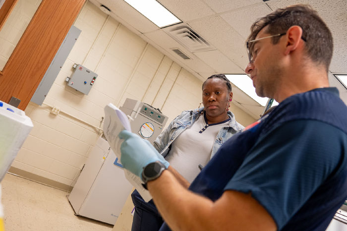 Two people stand in a lab, looking at a paper with instructions