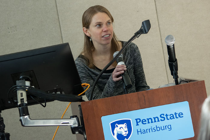 A woman speaks from behind a lectern, which has a Penn State Harrisburg logo on it