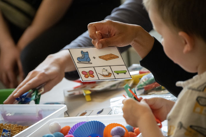A child looks at symbols on a card, with a sensory bin of cotton balsl in front of him
