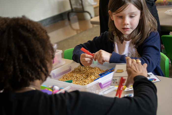 A child looks at symbols on a card, with a sensory bin in front of her