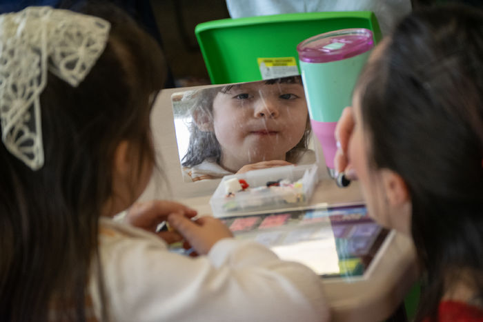 a child looks into a small mirror, lips pursed together