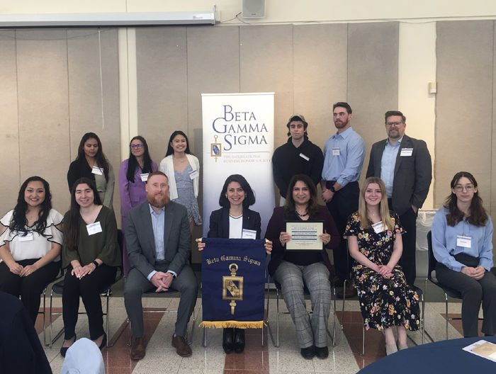 A group of people sitting and standing near a banner that says Beta Gamma Sigma