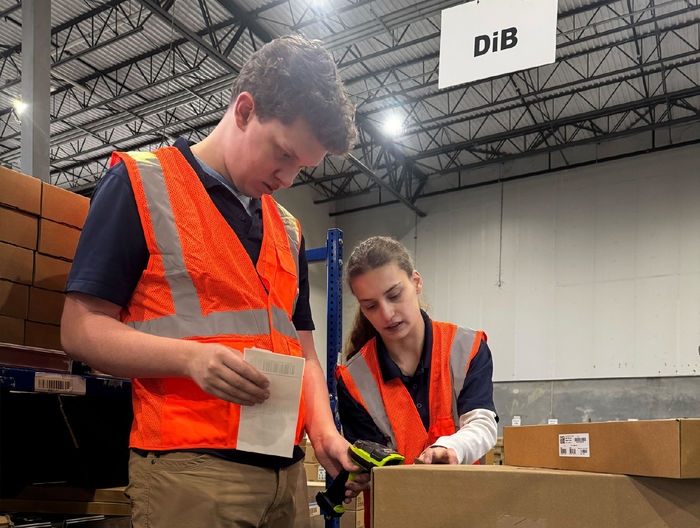 Two people in orange vests scan the barcode on a package in a workplace