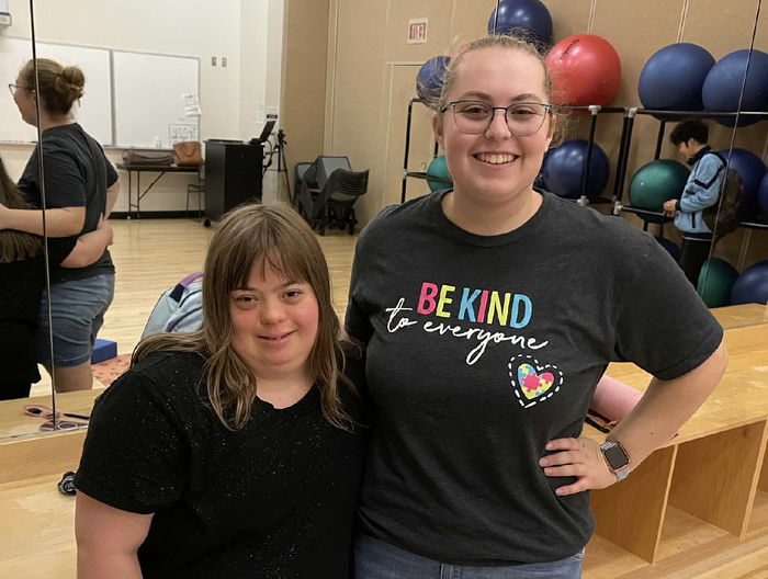 two women pose in a room with exercise equipment