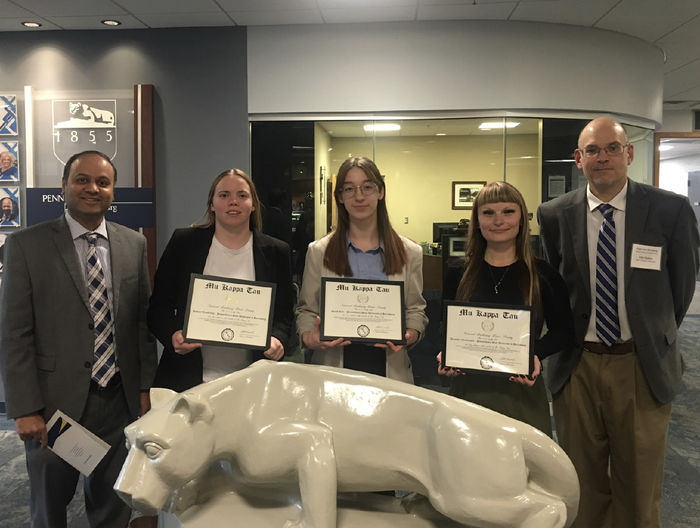 A group of people stand around the Nittany Lion statue in Olmsted Building. Three students hold certificates.