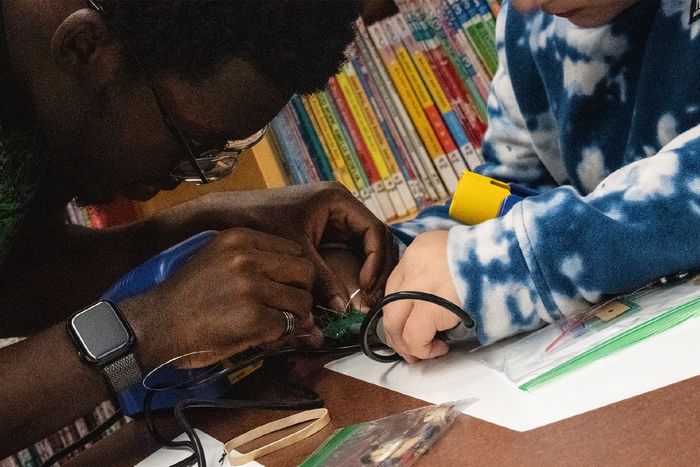 Close up photo of a college student helping a younger child with a soldering activity