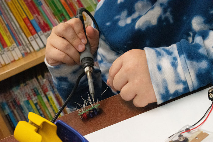 A middle school student holds a soldering iron during a Teen STEM program