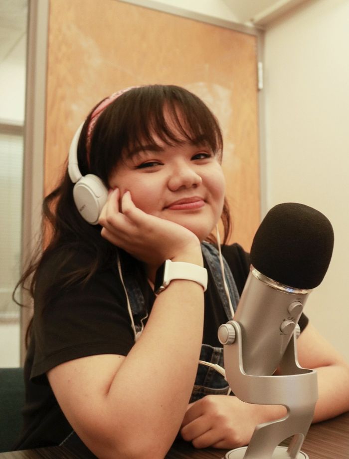 Victoria Pham sits with her chin resting in her hand, wearing a headset and sitting in front of a microphone.