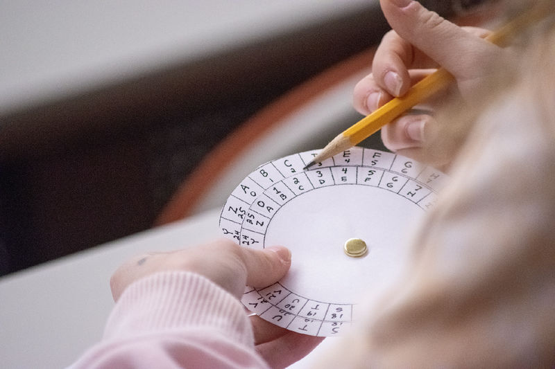 Closeup of a student's hands holding a pencil and a paper wheel with letters and numbers