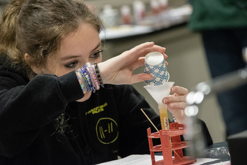 A student pours liquid into a test tube from a small paper cup