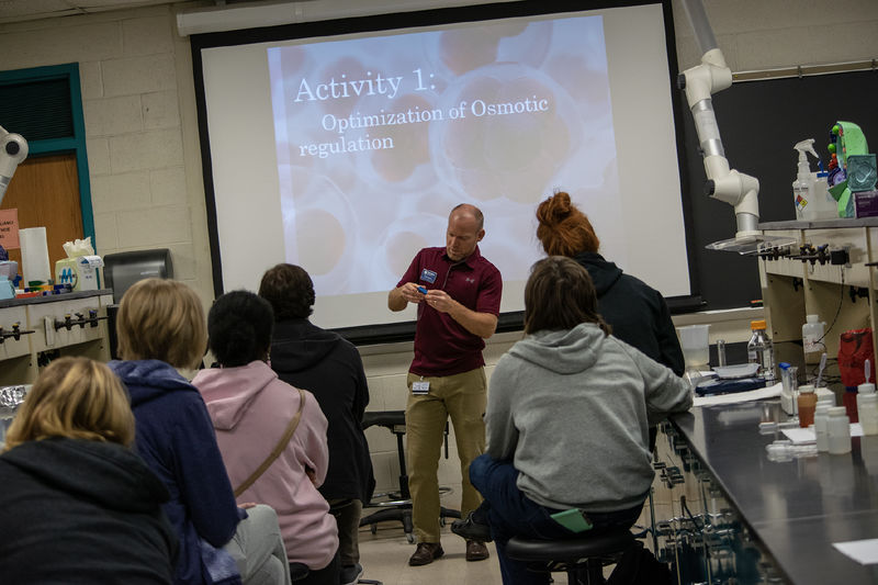 Students sit at lab tables while a man at the front of the room gives instructions during a biology workshop