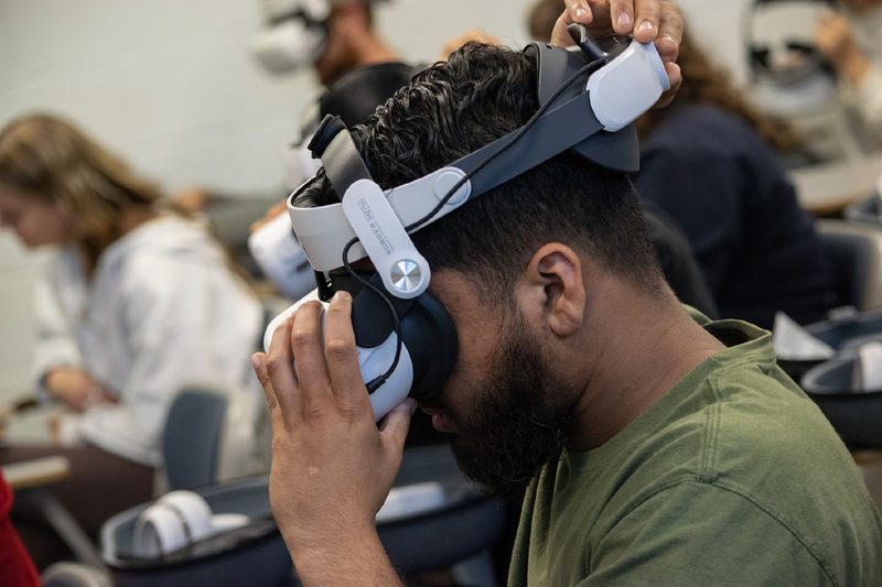A student adjusts a virtual reality headset that is strapped to his head