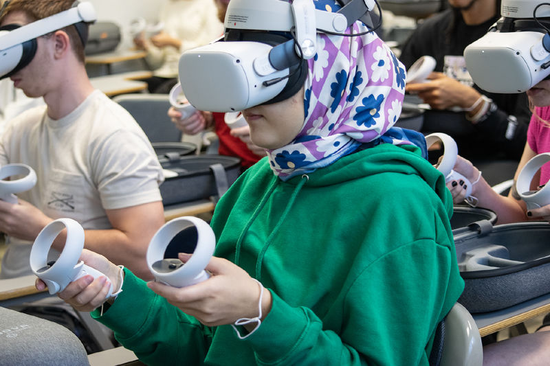 A student wears a virtual reality headset and holds a controller in each hand