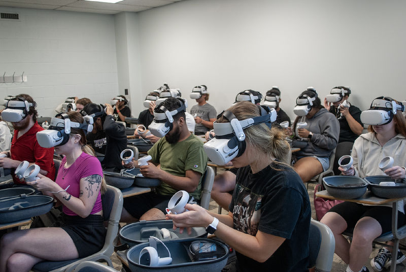 A classroom full of students wearing virtual reality headsets and holding the controllers