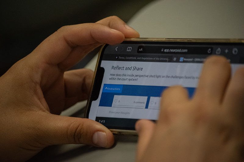 Closeup of a student's hands holding a phone with a reflection question on the screen