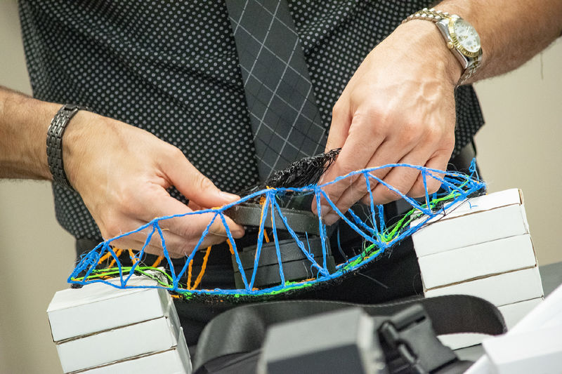 Closeup of hands placing weights onto a 3D printed bridge