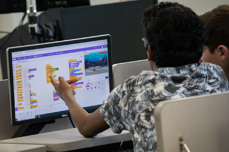 A student points to a computer screen showing a colorful coding activity