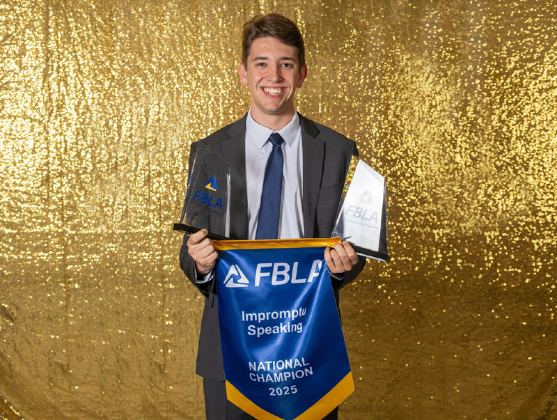 Aiden Beiler holds a flag that says FBLA National Champion Impromptu Speaking