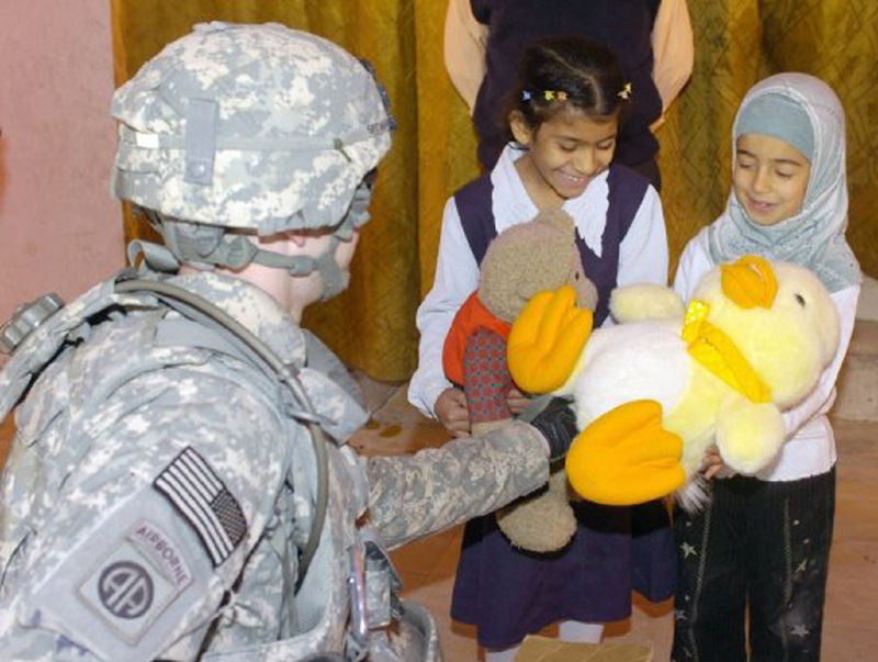 A man in an Army uniform hands stuffed animals to children