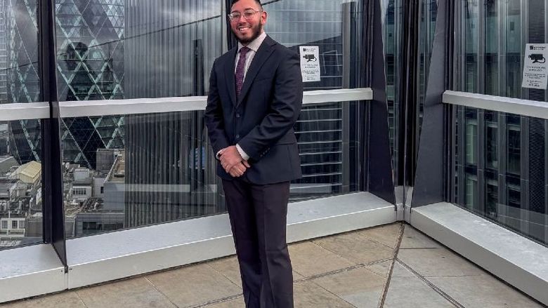 A student wearing a suit stands on a rooftop in London
