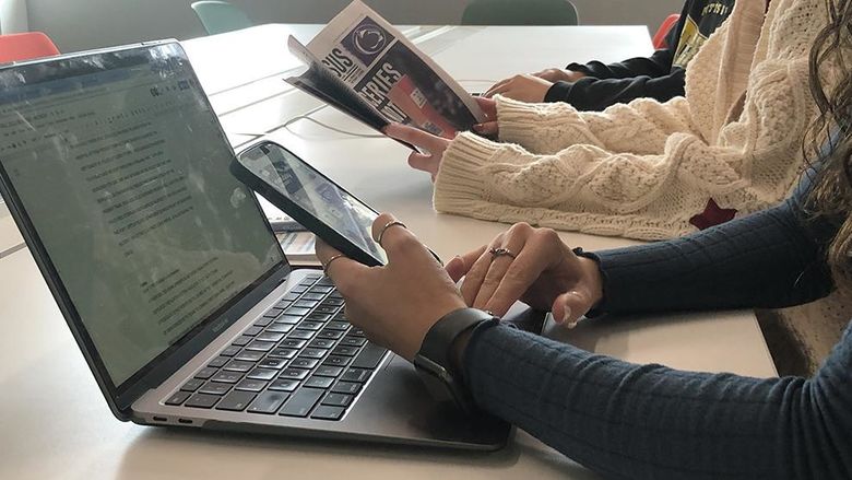 Students at laptop, with smartphone and newspaper