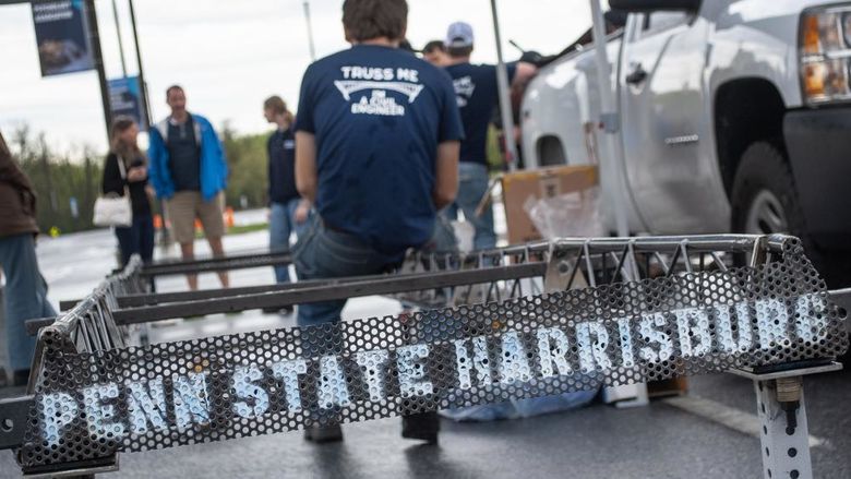 A student sits on the edge of a steel bridge that has "Penn State Harrisburg" painted on it