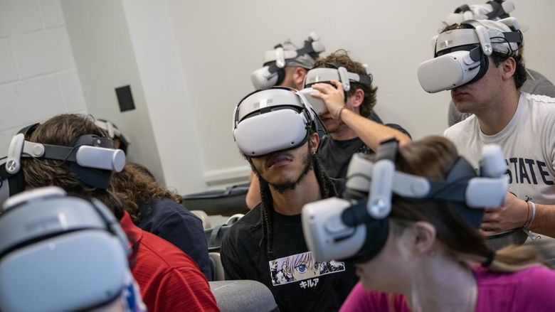 Students in a classroom wear white reality headsets that cover their eyes