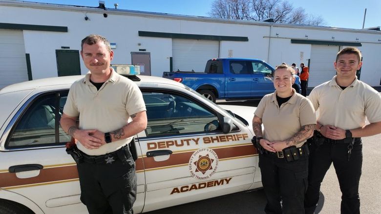 Three people standing in front of a deputy sheriff academy vehicle