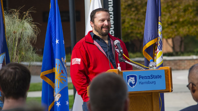 Photo of Ryan Allman, standing behind a lecturn and in front of flags during a 2021 Veterans Day ceremony 