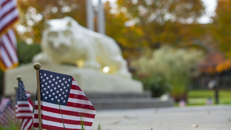 Photo of U.S. flags planted in the grass, with the Nittany Lion statue in the background