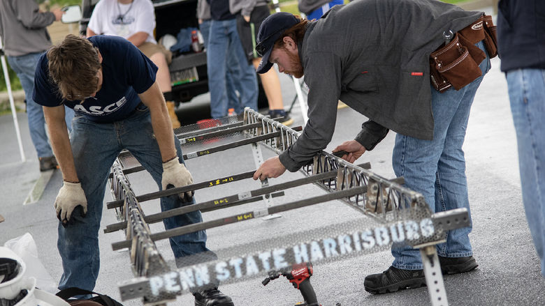 Two students work on a steel bridge during the ASCE competition