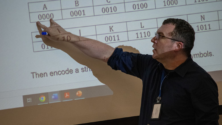Craig Culbert, assistant teaching professor of mathematical sciences at Penn State Harrisburg, points to information on a large screen.  