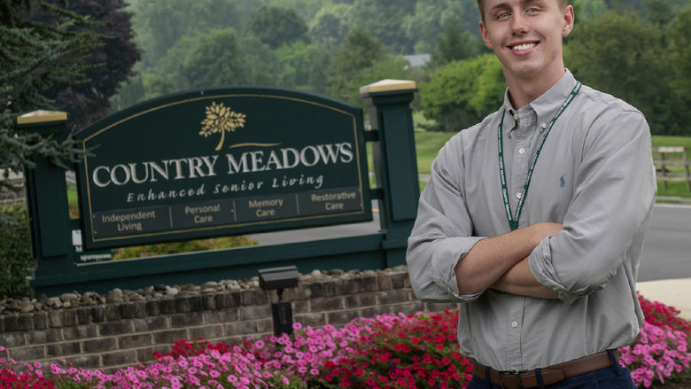 Brennan Quigley stands in front of a sign for Country Meadows