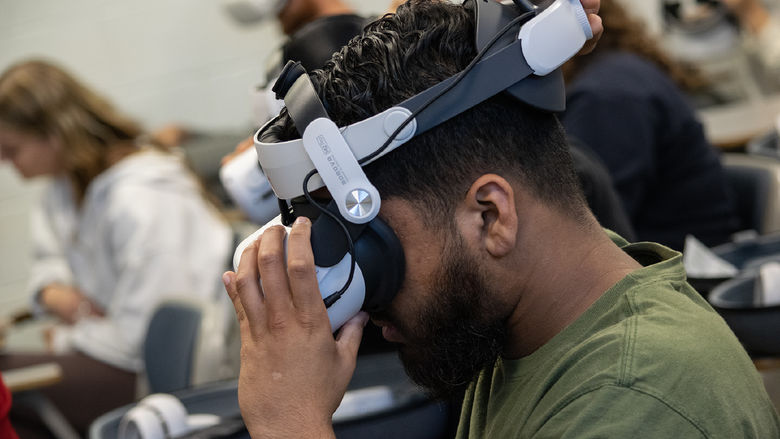 A student adjusts a virtual reality headset that is strapped to his head