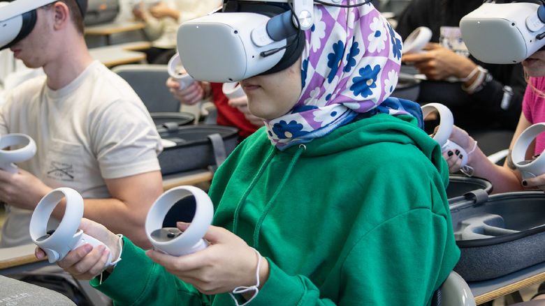 A student wears a virtual reality headset and holds a controller in each hand