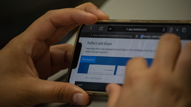 Closeup of a student's hands holding a phone with a reflection question on the screen