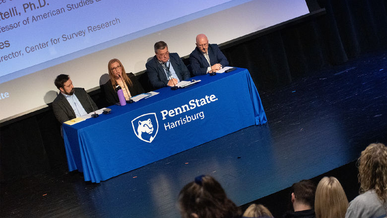 A photo of four people sitting behind a table during a presentation on a stage